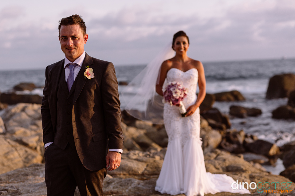 Nice Shot Of The Handsome Groom On The Rocks With His Bride In The Background