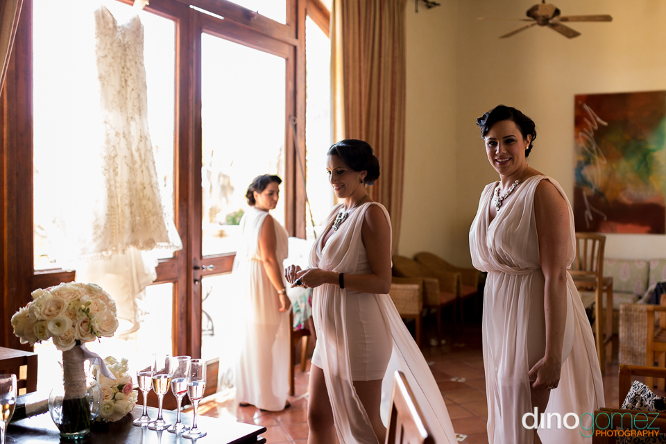 A Shot Of The Bridesmaids In Their Hotel Room With The Wedding Dress Hanging By The Door