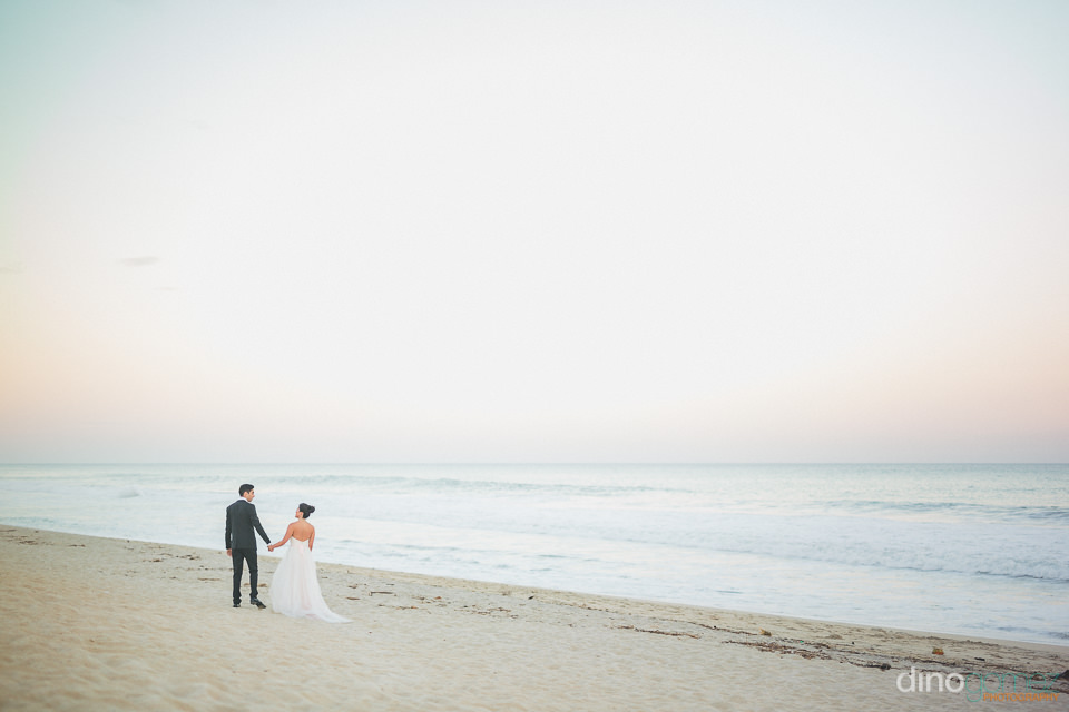 Long Shot Of Newlyweds Walking On The Beach In Suit And Dress Ne