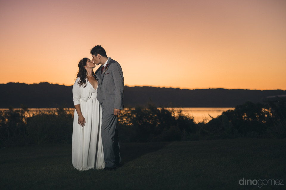 newlyweds kiss in front of lake at sunset in romantic wedding ph
