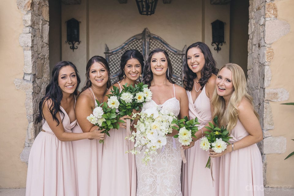 Pretty Bride And The Bridemaids Are Posing Beautifully For The Camera All Well-Dressed For The Wedding Ceremony- Nicole & Ryan	Bride Dressed In Cream Lace Gown And The Bridemaids In Smiliar Colored Dress Are Posing Beautifully For The Camera Infront Of A
