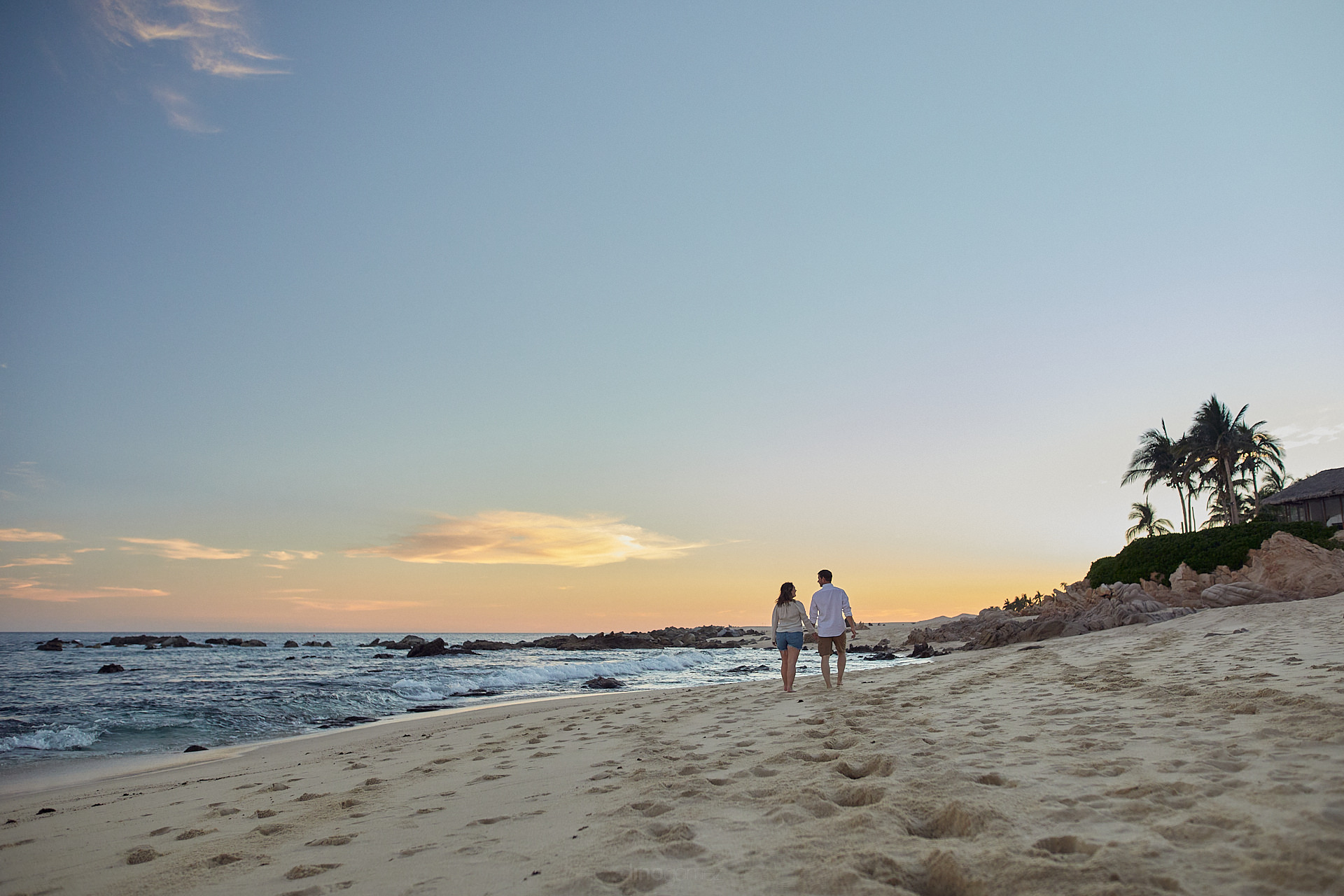 two people walking on a beach at sunset.