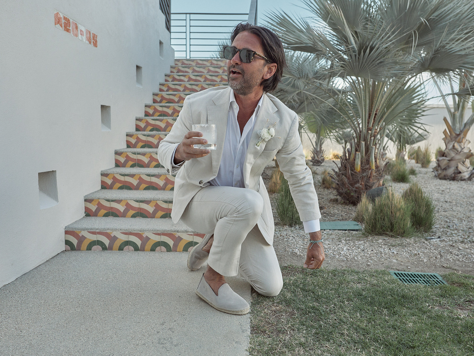 A Man In A White Suit Is Holding A Drink.