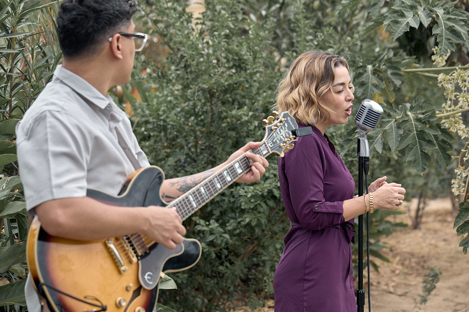 A man and woman singing and playing guitar in a field.