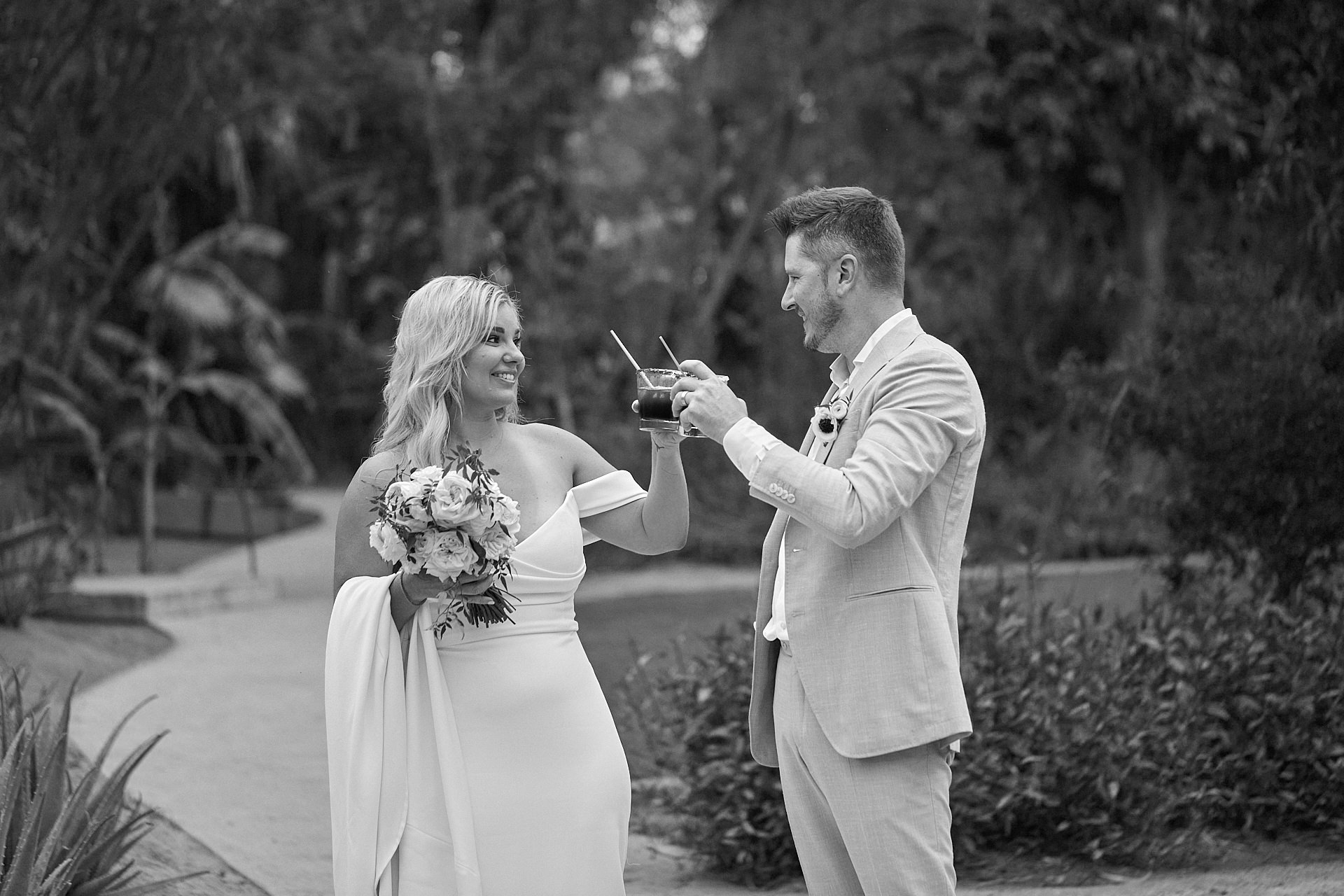 A black and white photo of a bride and groom sharing a glass of wine.