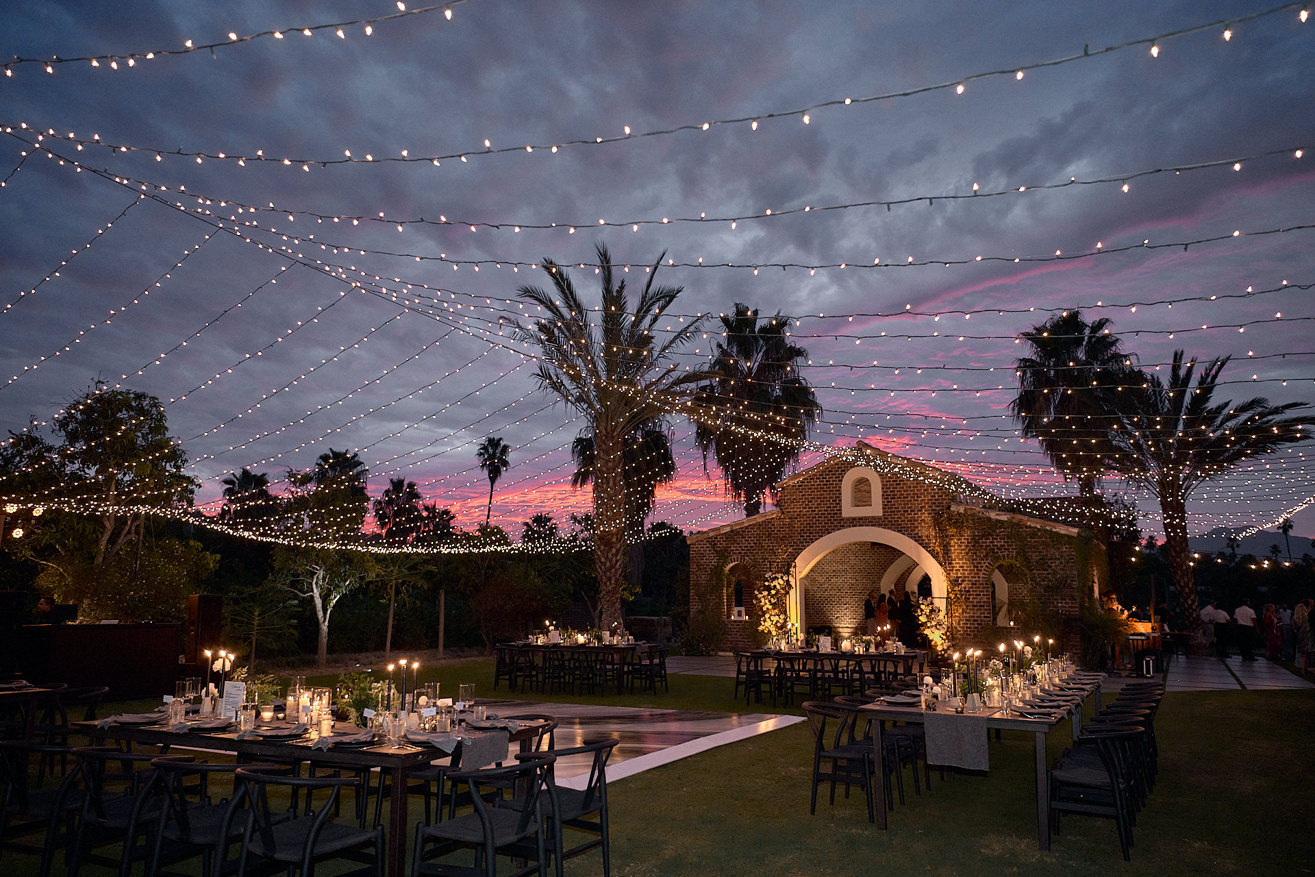 An outdoor wedding reception with string lights and palm trees.